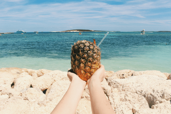 ruky drziace drink v ananase na piesocnatej plazi